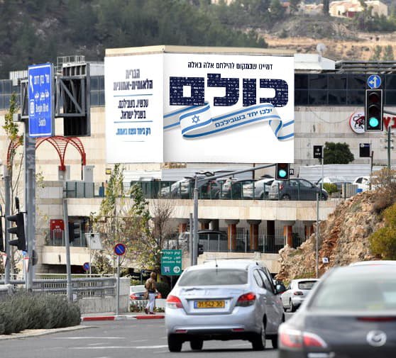 שלט חוצות של הקמפיין בצומת עירונית, ועליו הכיתוב דמיינו שבמקום להילחם אלה באלה, המילה כולם, וסרט דגל ישראל. לצידו לוח נוסף ובו שם הברית הלאומית-אמונית והמשפט עכשיו, בשבילכם, בשביל ישראל.